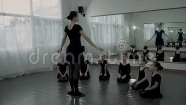 芭蕾舞女站在几个看着她的小芭蕾舞女演员面前。 成人芭蕾舞者教丽特尔芭蕾舞者如何移动